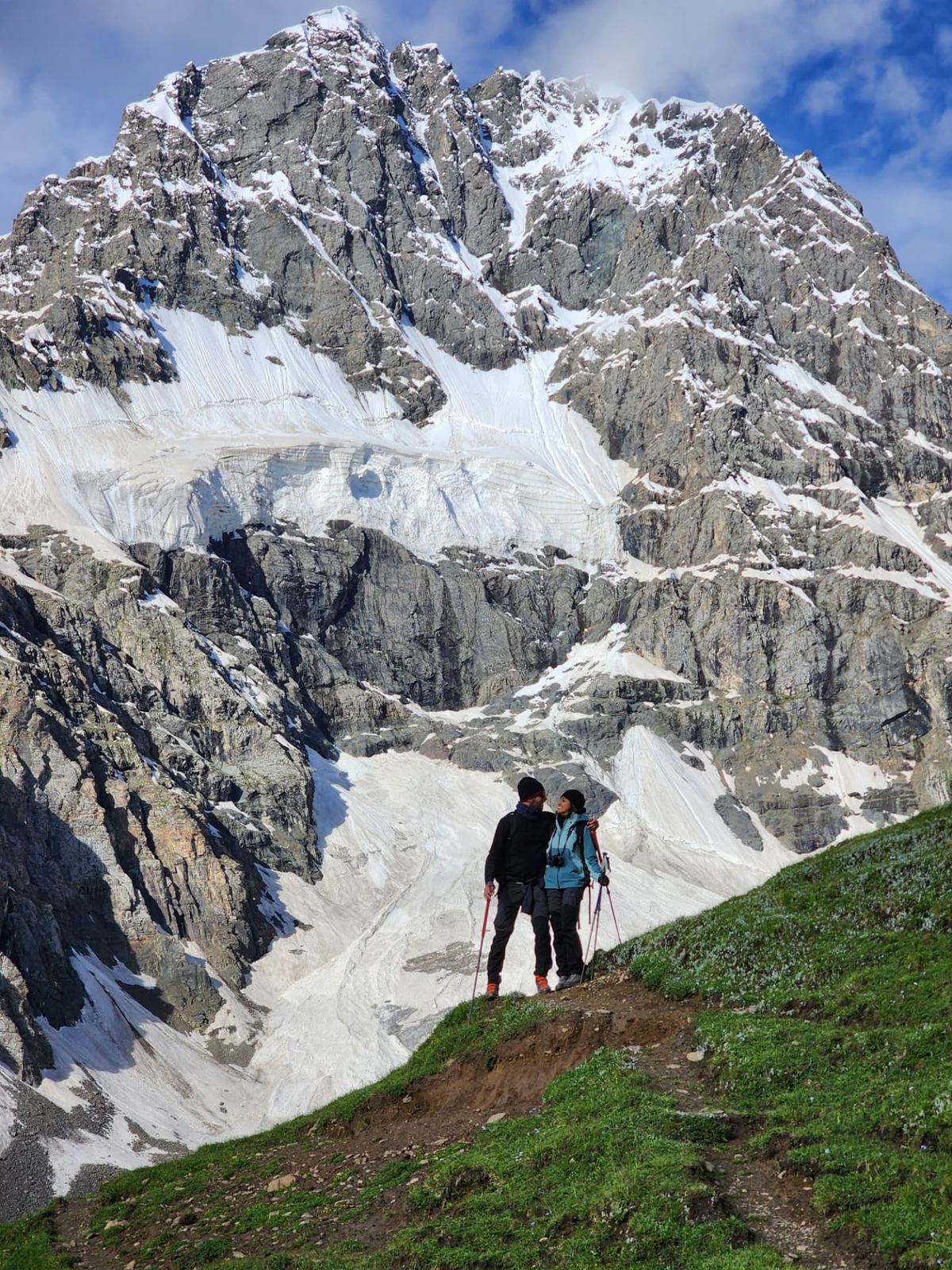 Travellers on a green hillside below a snow-capped Karakoram giant