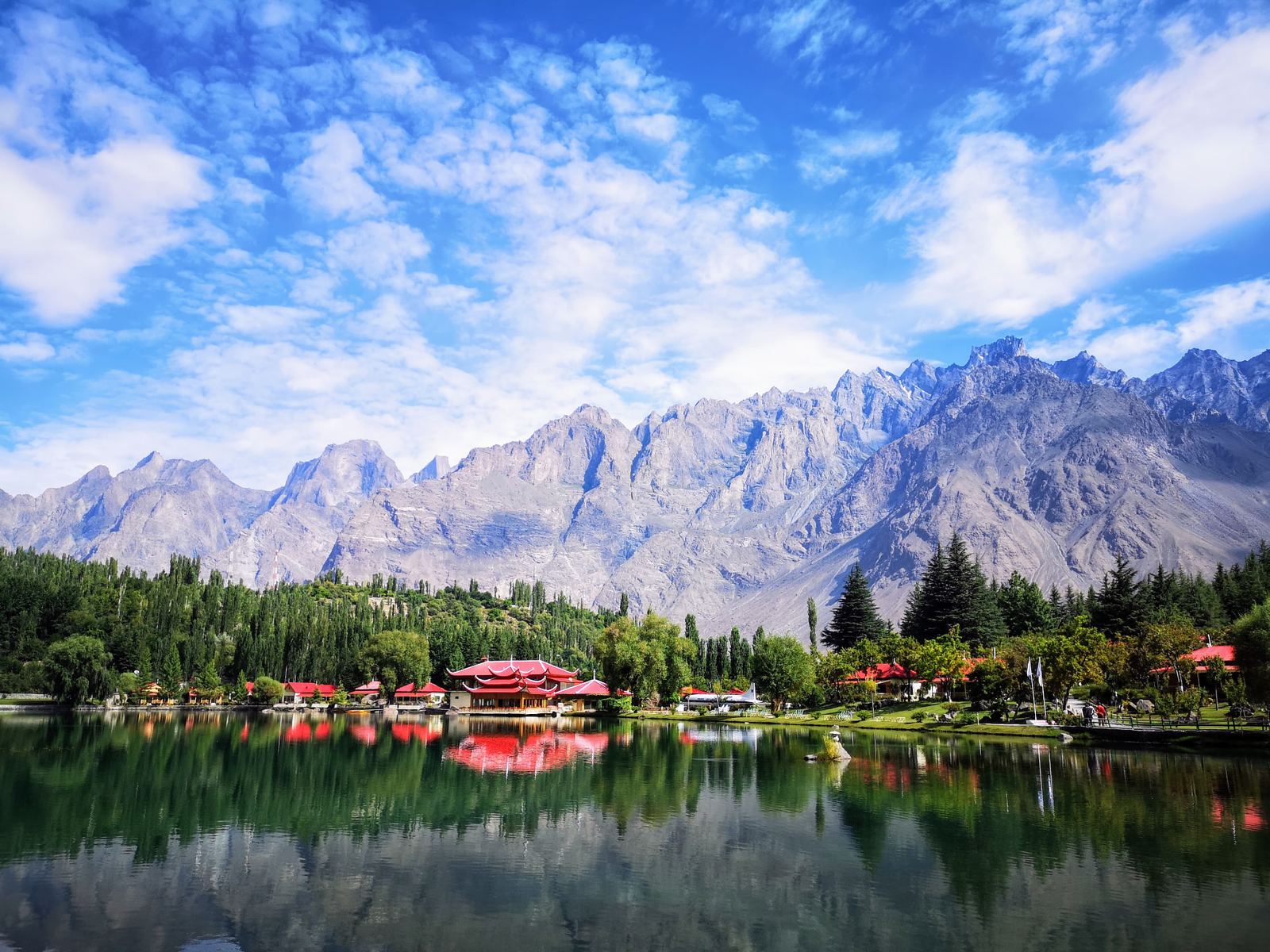 Mirror-still lake reflecting village rooftops and Karakoram peaks